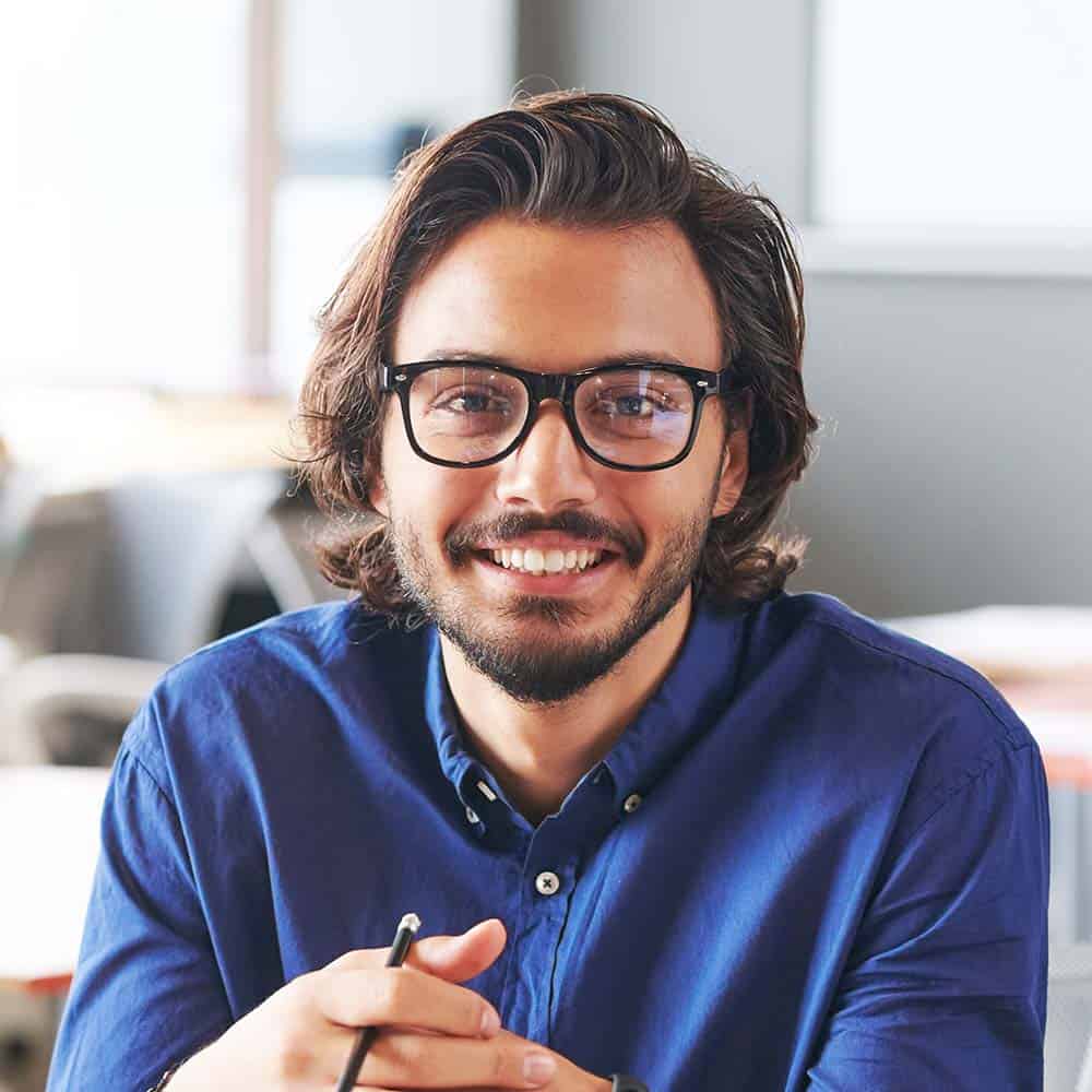 Smiling man with glasses in a modern office environment.